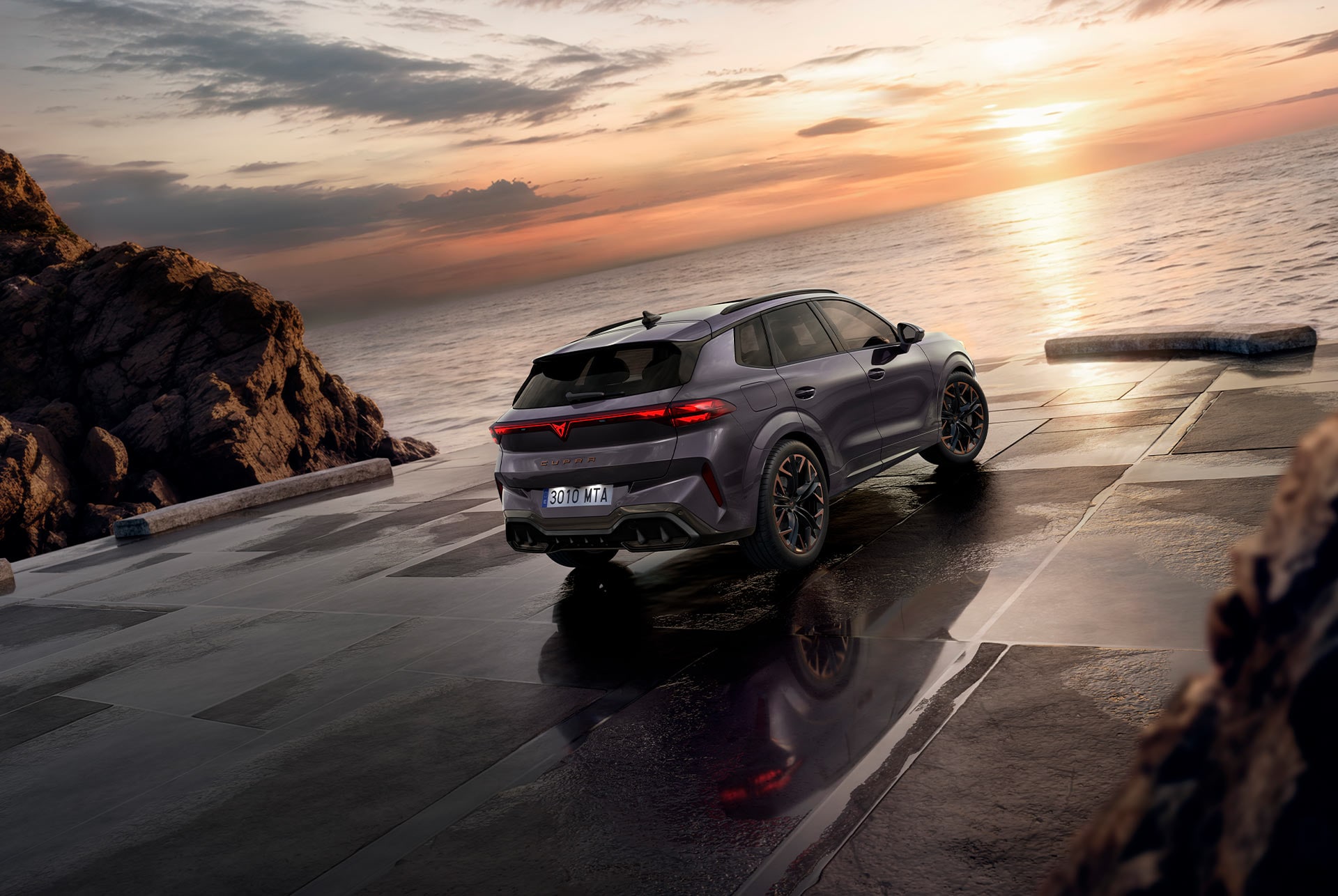 SUV híbrido CUPRA Terramar, nuevo modelo 2024, ángulo de visión trasera, con elegantes faros traseros con el logotipo de CUPRA, modernas llantas de aleación y una carrocería deportiva, sobre una acera mojada junto al mar. 