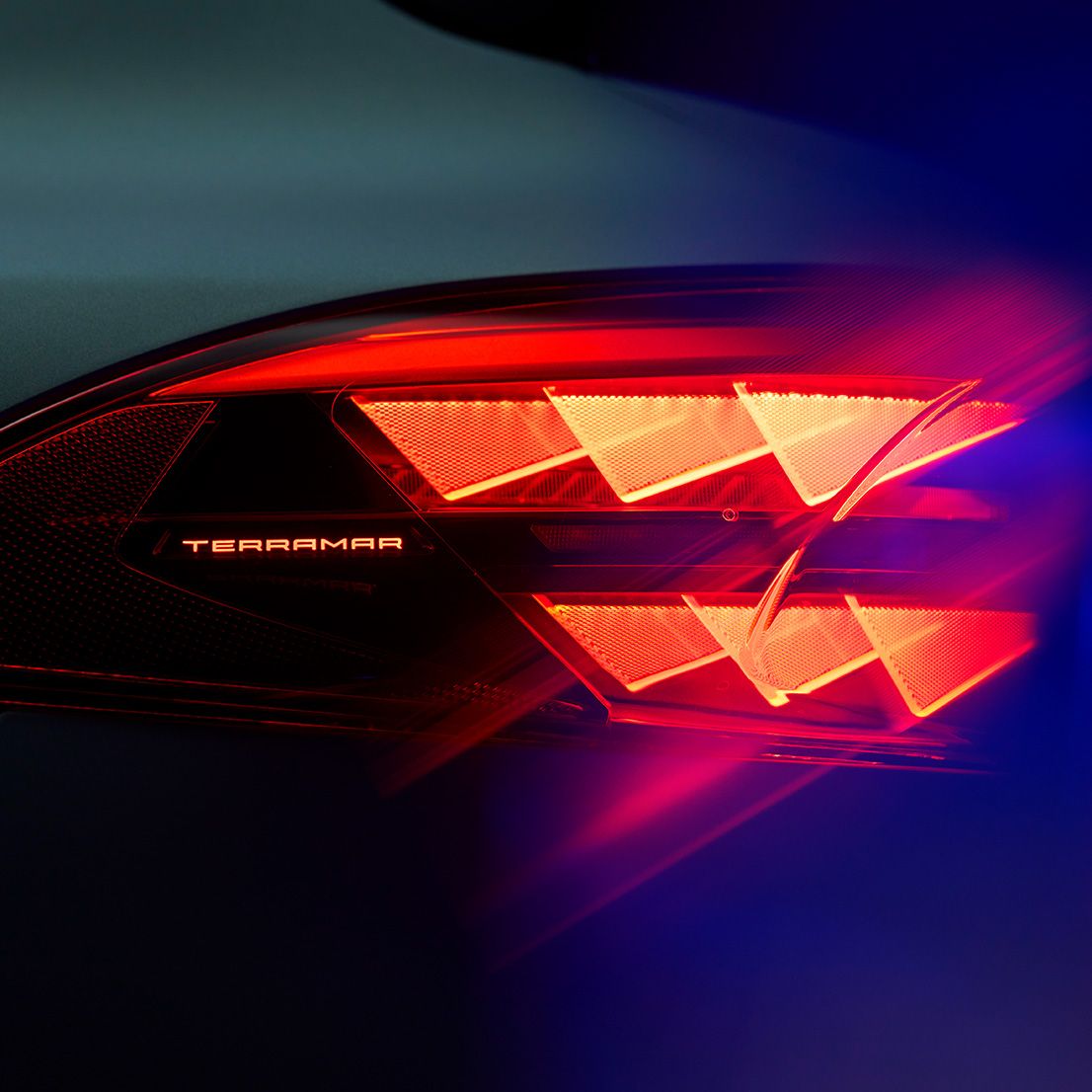 Primer plano de la luz trasera del nuevo CUPRA Terramar con el nombre del modelo iluminado, mostrando un distintivo patrón de luz triangular rojo contra un fondo oscuro.