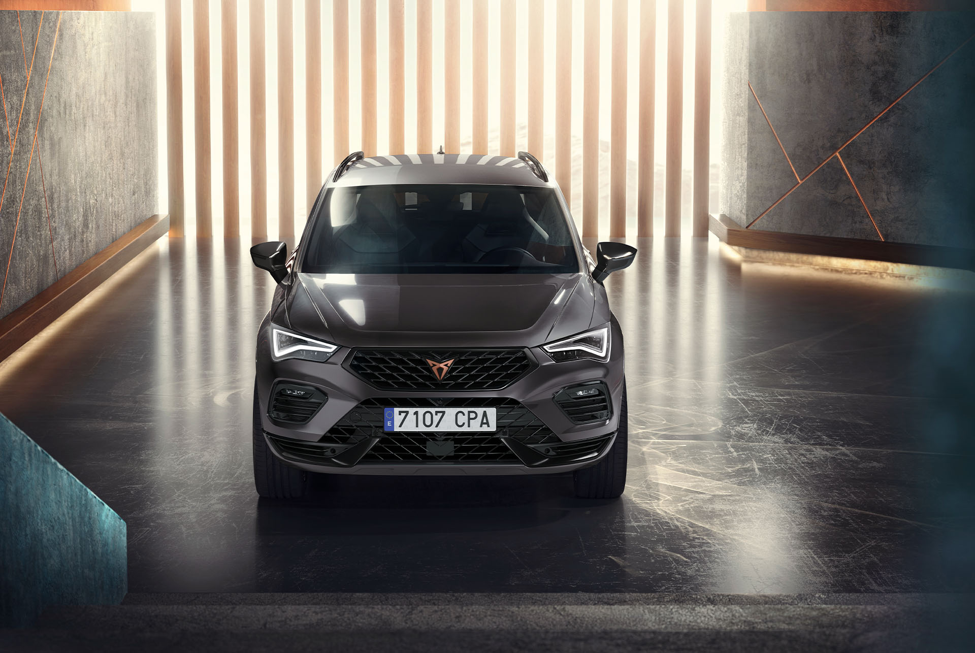 Vista frontal del CUPRA Ateca, un SUV gris, en un entorno moderno e iluminado. En la imagen destaca la atrevida parrilla delantera, los faros LED y el elegante diseño del coche. 