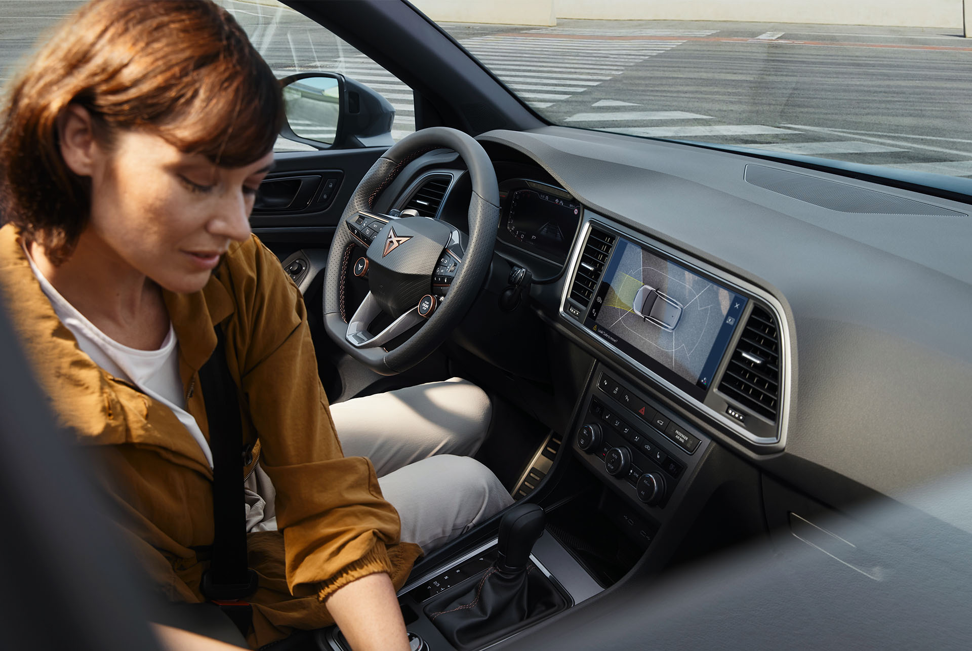 El interior del CUPRA Ateca destaca por sus avanzadas prestaciones tecnológicas. El salpicadero tiene una gran pantalla de Infotainment con navegación y el volante con botones satélite cuenta con controles integrados. Dentro hay una mujer sentada. 