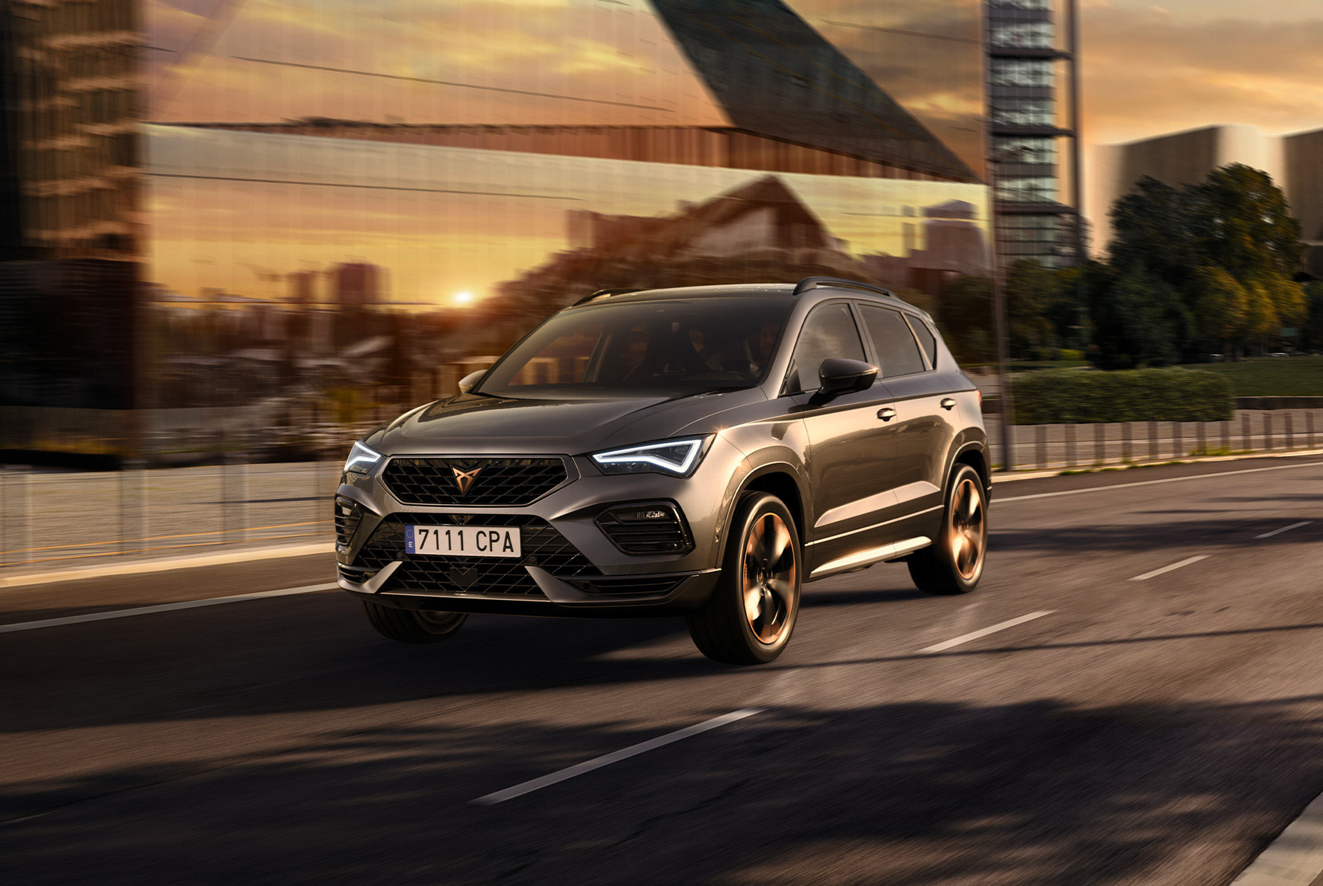 Un CUPRA Ateca SUV gris sobre fondo blanco. El coche presenta una llamativa calandra delantera, faros LED y llantas de aleación con detalles en cobre, que resaltan su diseño de coche deportivo.