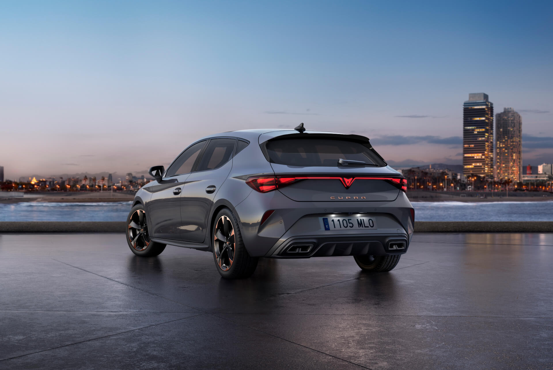 Vista trasera del nuevo modelo de coche CUPRA León 2024 gris brillante con control de chasis adaptativo y llantas de aleación en negro y cobre. Ciudad al fondo al atardecer.