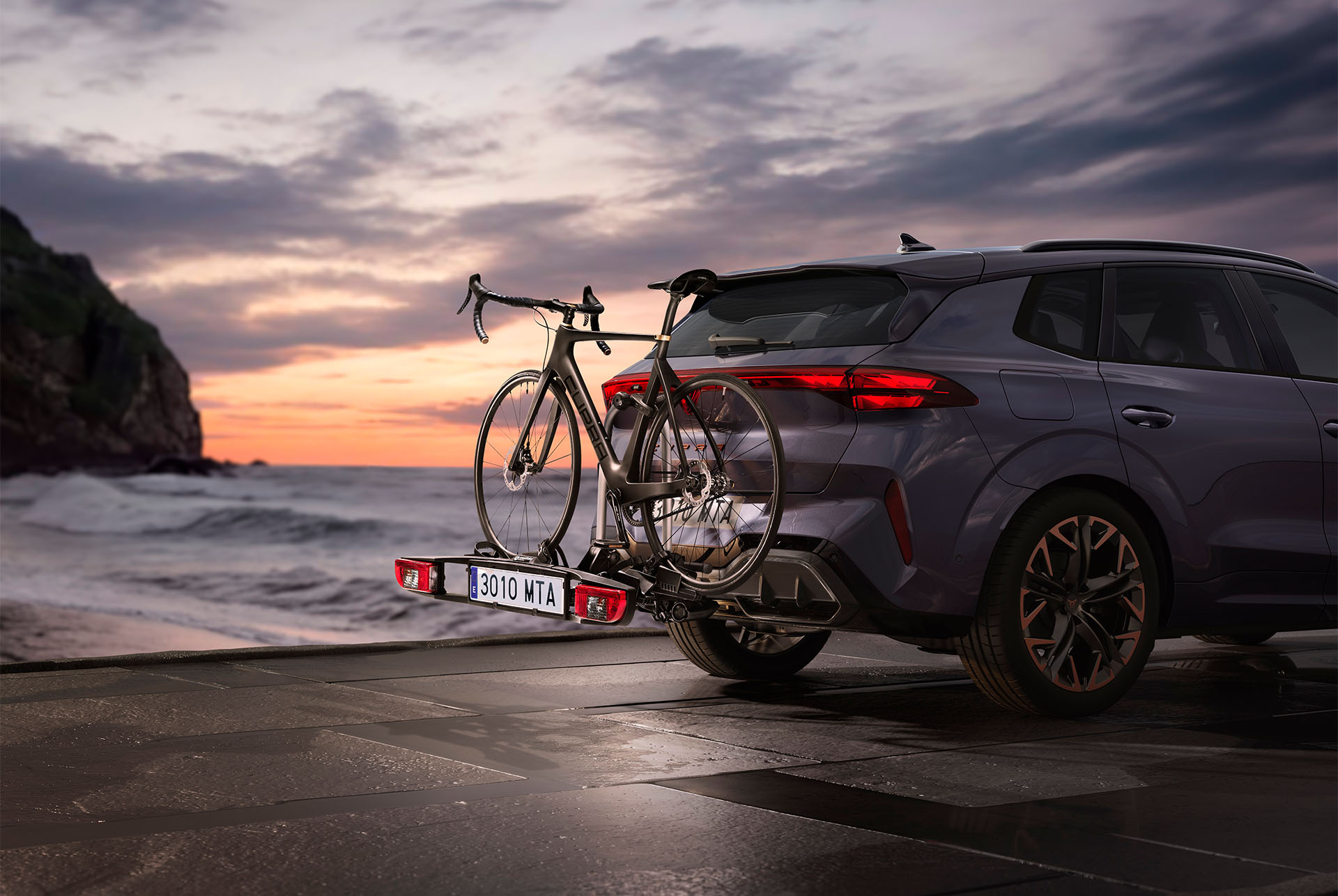 CUPRA Tow Bar Bicycle Rack with two bikes attached, parked by the coast at sunset. The tow bar carrier provides a convenient and secure option for transporting bikes, capable of handling up to 60kg. 