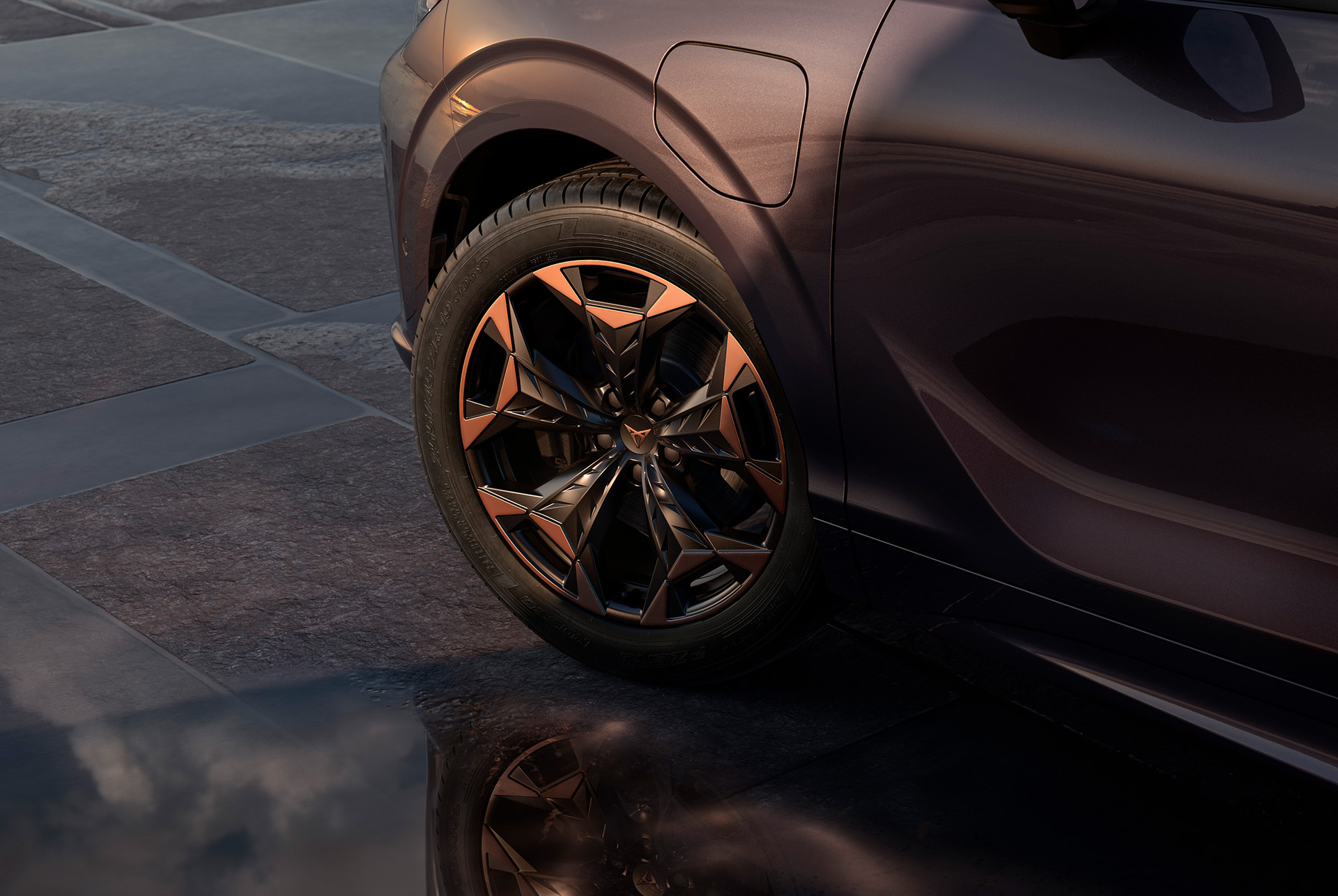 Llantas de aleación Cosmic Copper de 48 cm (19") en negro con detalles en cobre en el nuevo CUPRA Terramar. En el fondo hay una acera de baldosas y parte de la carrocería brillante y oscura del coche.