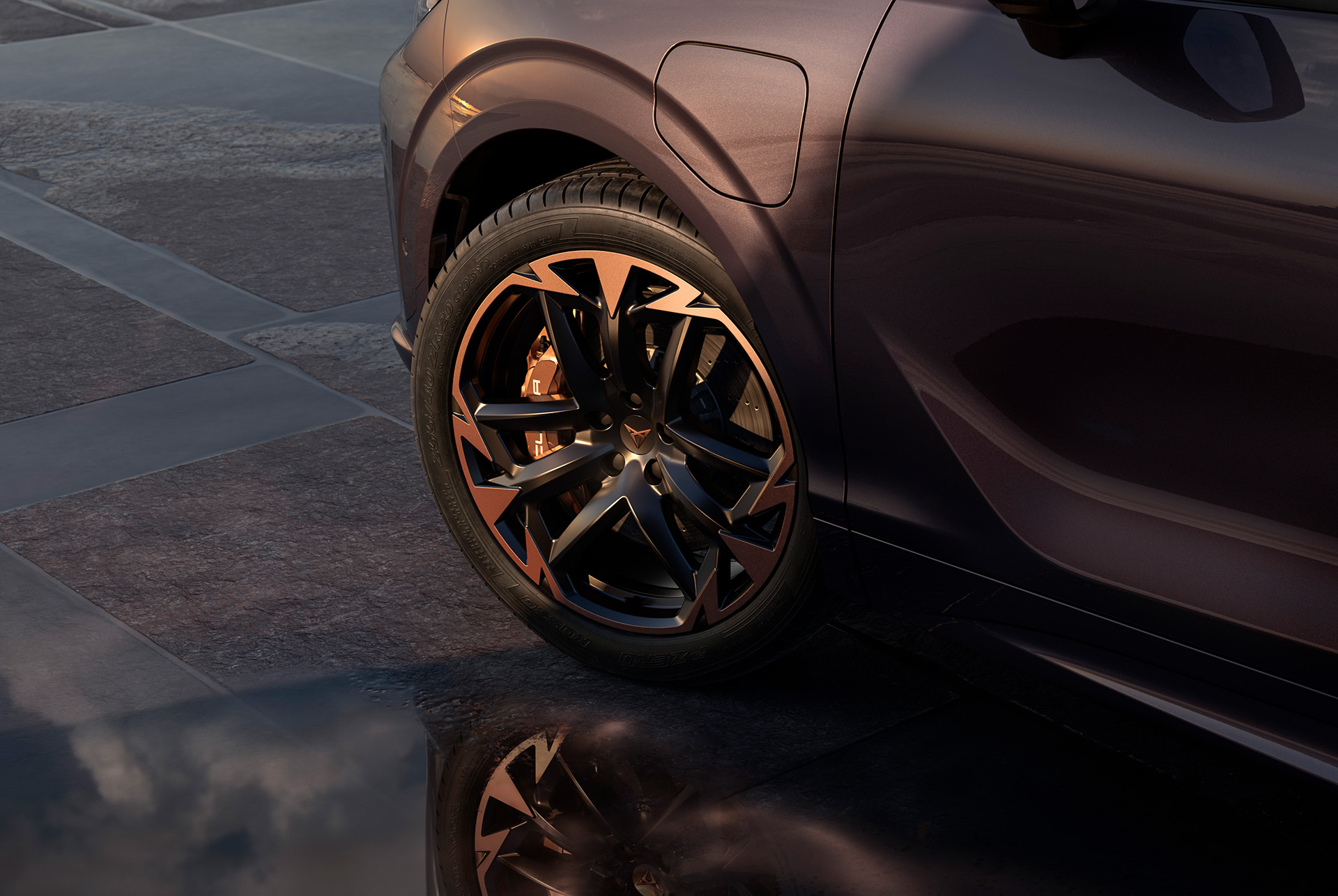 Llantas de aleación Vortex Copper de 50,8 cm (20") en negro con detalles en cobre en el nuevo CUPRA Terramar. En el fondo hay una acera de baldosas y parte de la carrocería brillante y oscura del coche.