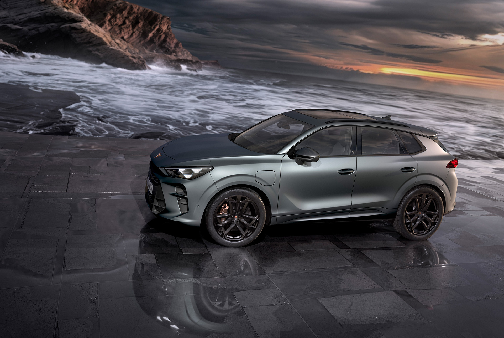 SUV híbrido CUPRA Terramar, nuevo modelo 2024, vista lateral, con llantas de aleación America’s Cup de 20 pulgadas y frenos Akebono, gris Enceladus mate, sobre una acera mojada junto al mar al atardecer.