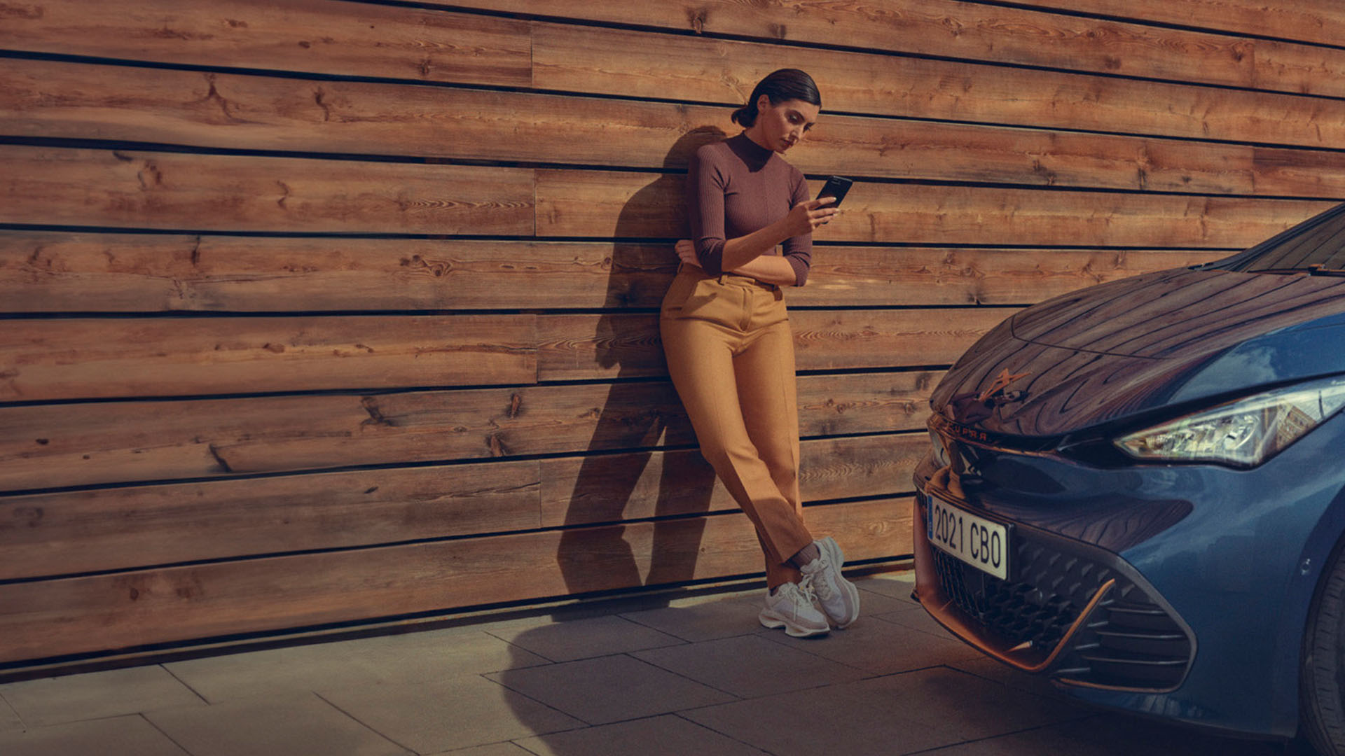woman standing next to a cupra born car with a phone