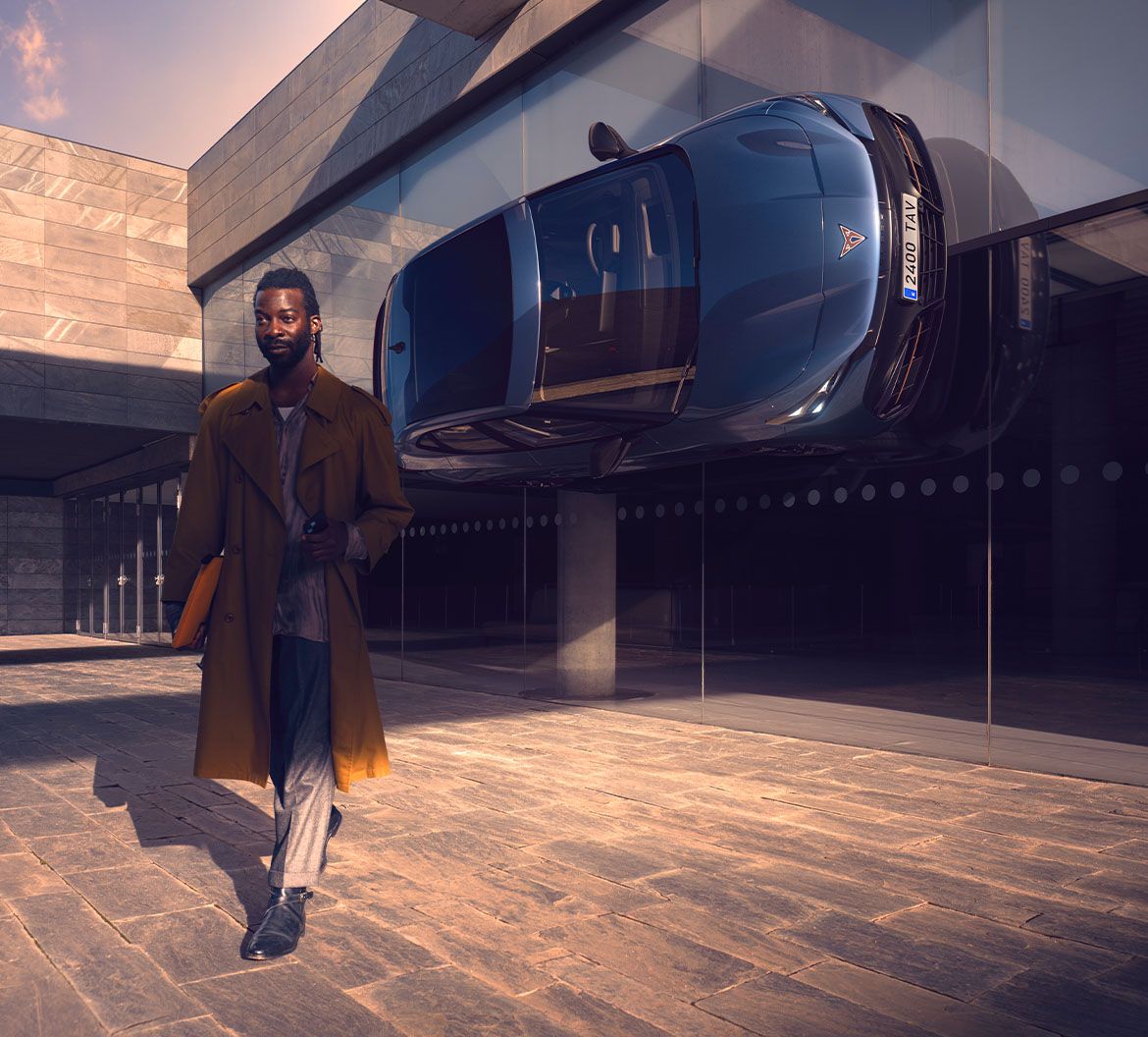 A person walks confidently beside a reflective building, with a cupra tavascan displayed, highlighting incentives for purchasing an electric car.